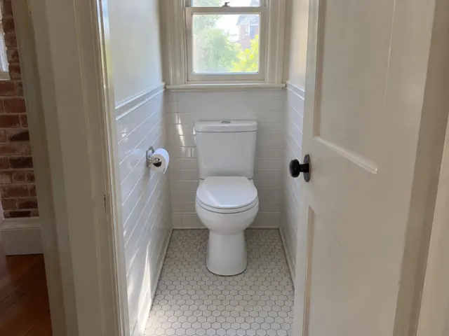 Clean white toilet in a small tiled bathroom with a window and open door in Newtown