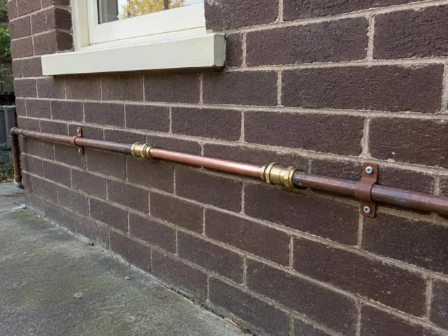 Copper water pipe repair along a brick exterior wall beneath a window in Stanmore